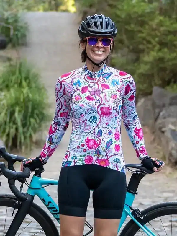 Woman in colorful floral cycling jersey and black shorts, standing with turquoise road bike outdoors