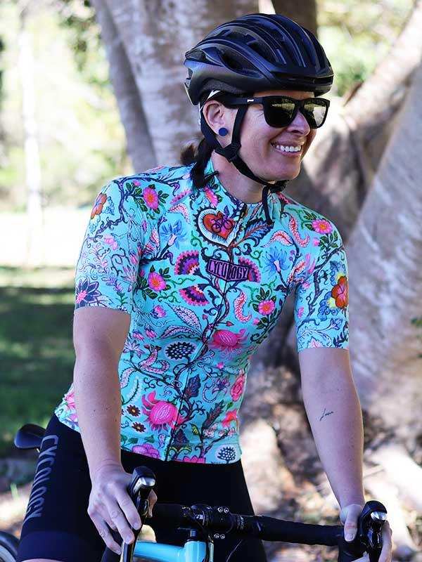 Woman cycling in vibrant floral jersey and black helmet, outdoors on sunny day