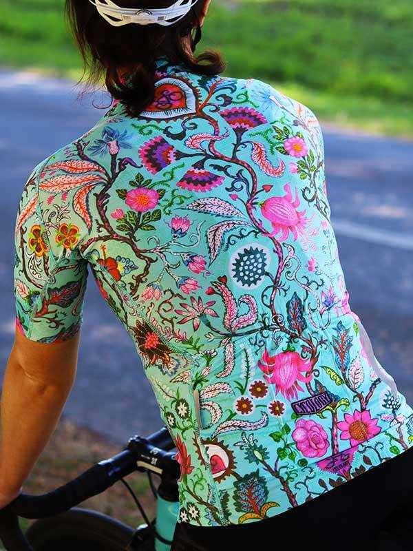 Woman cycling in vibrant floral print jersey, colorful botanical design on teal background