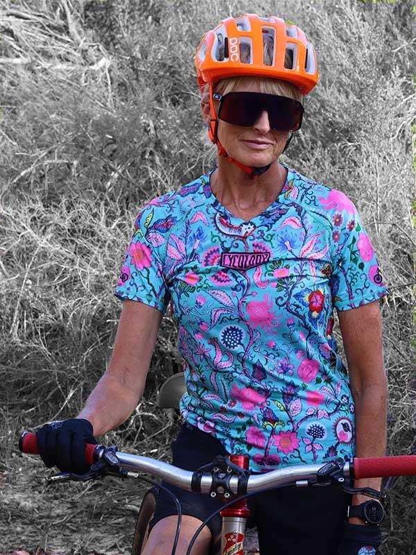 Woman in floral cycling jersey and orange helmet riding mountain bike outdoors
