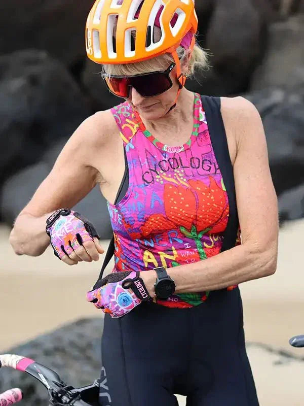 Woman in colorful cycling jersey and orange helmet checking smartwatch on beach