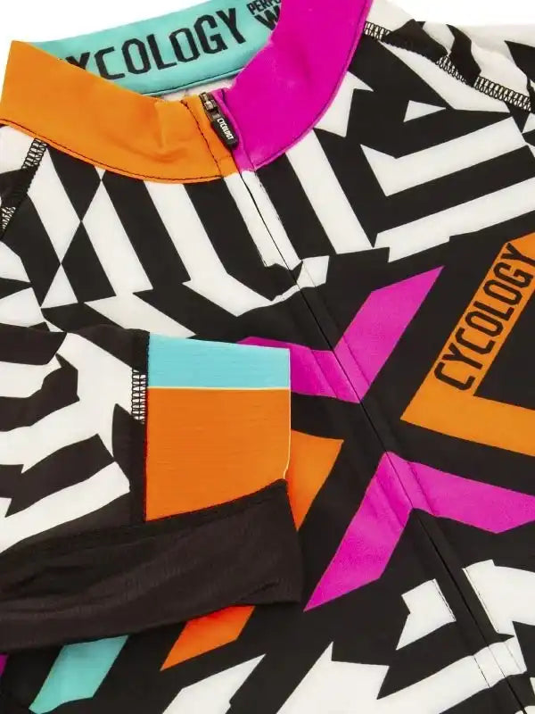 Vibrant geometric cycling jersey with bold black, white, pink, orange, and teal patterns, featuring zippered pockets and branded collar.