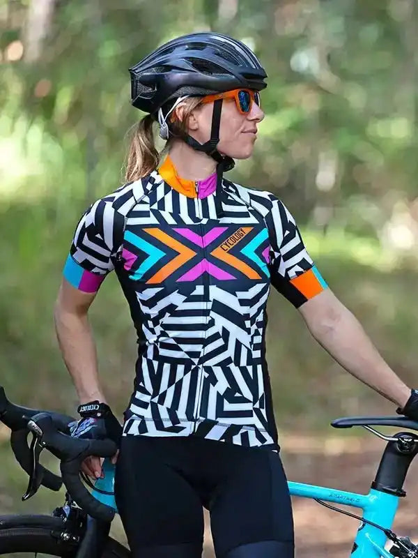 Woman in geometric pattern cycling jersey and helmet, standing with road bike outdoors