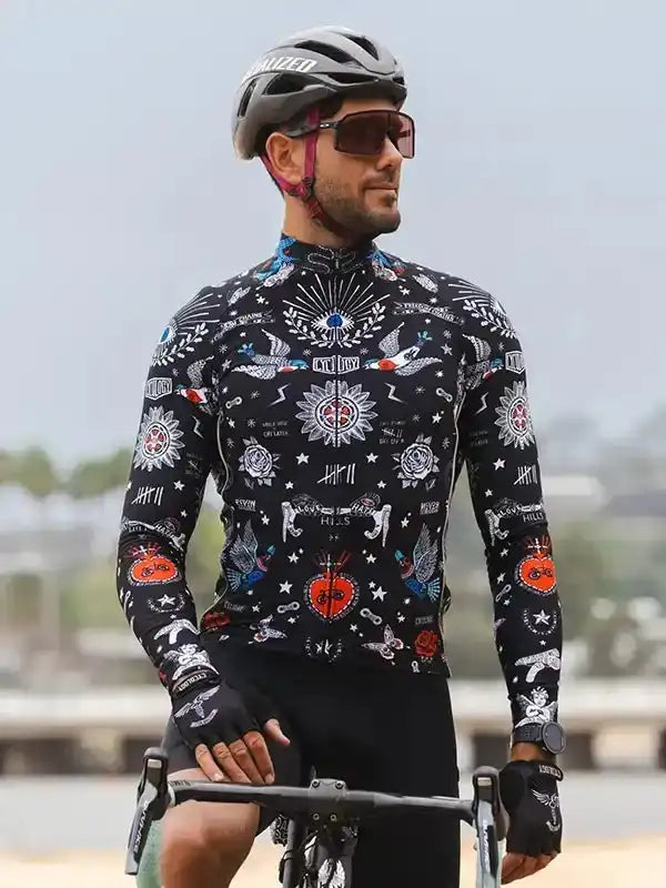 Man wearing black long-sleeve cycling jersey with tattoo-style graphics, helmet, and sunglasses outdoors